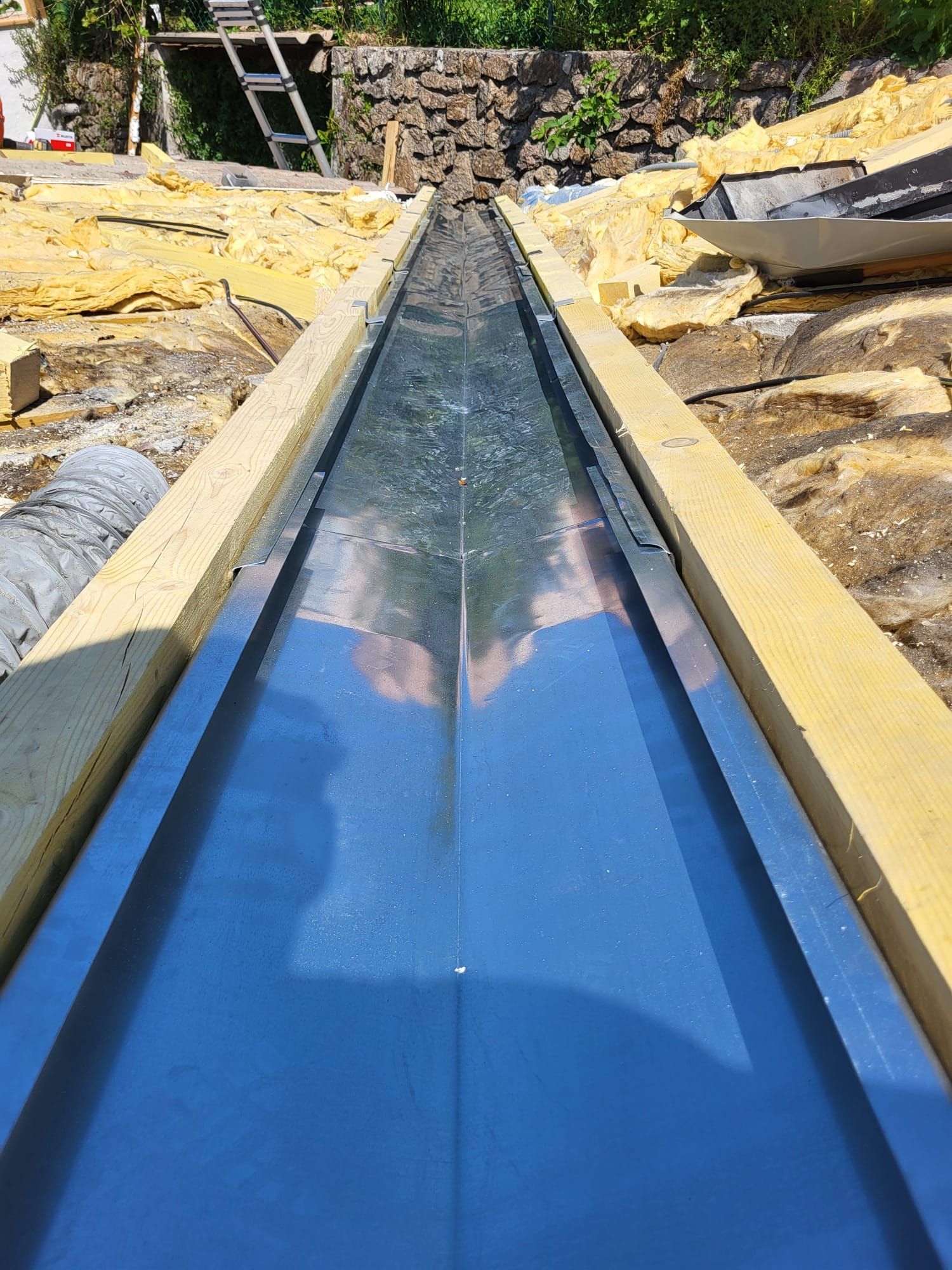 Gouttière métallique en cours de construction, flanquée de supports en bois et d'isolant.