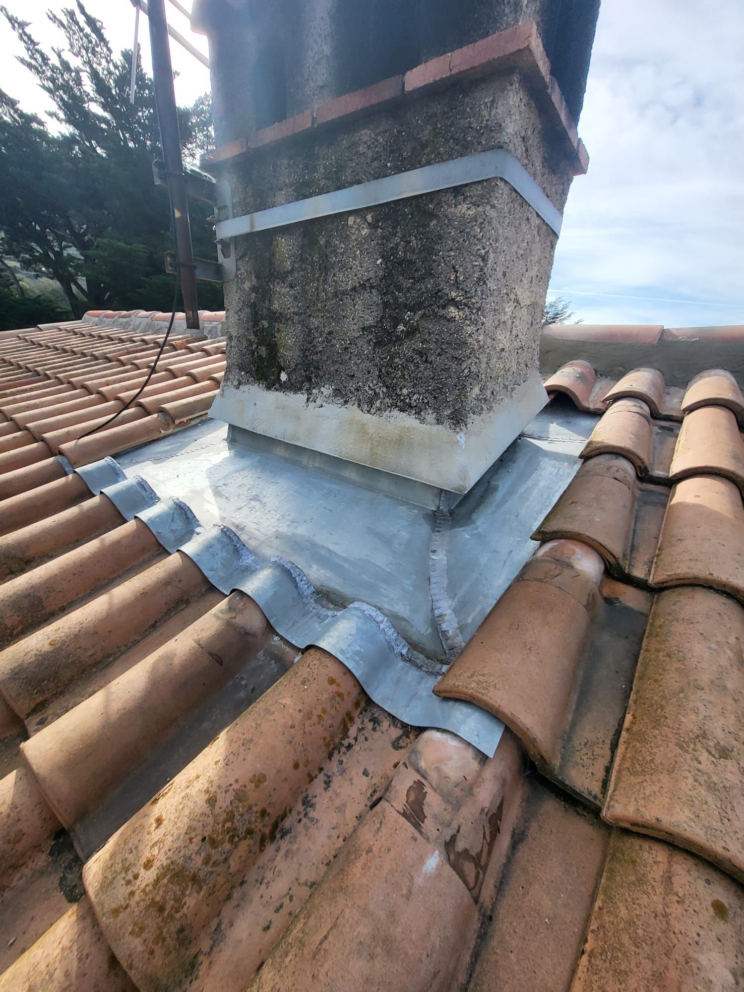 Cheminée sur un toit de tuiles rouges, avec solin en plomb à la base.