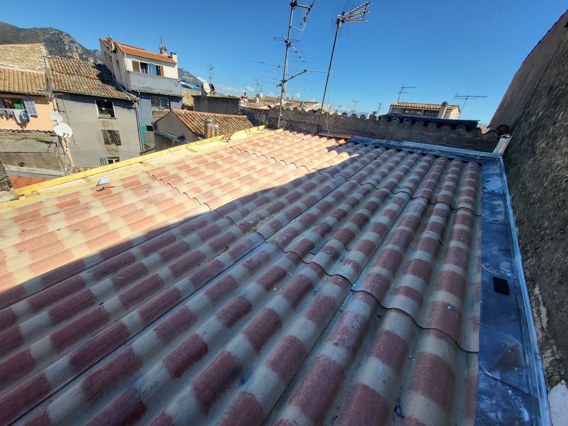 Toit en tôle ondulée rouge avec un paysage urbain en arrière-plan sous un ciel bleu dégagé.
