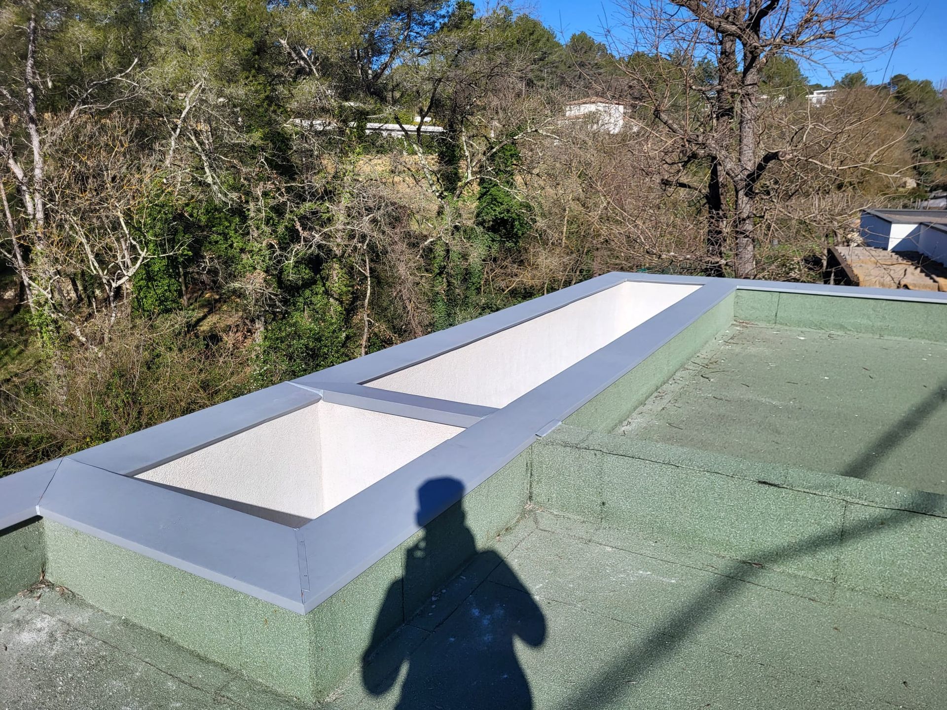 Puits de lumière sur un toit plat. L'ombre d'une personne se projette sur le toit végétalisé. Arbres et ciel en arrière-plan.