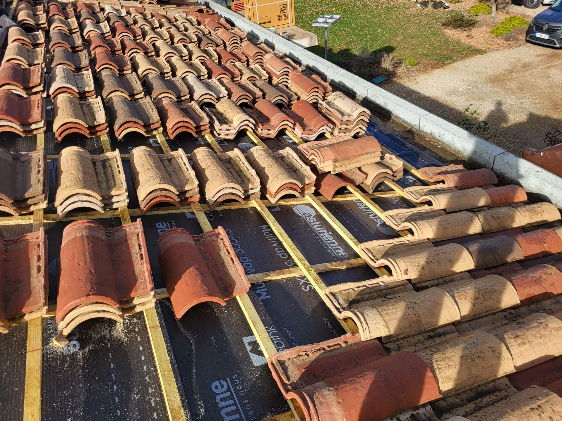 Pose de tuiles en terre cuite sur un toit dont la sous-couche et les liteaux en bois sont visibles.