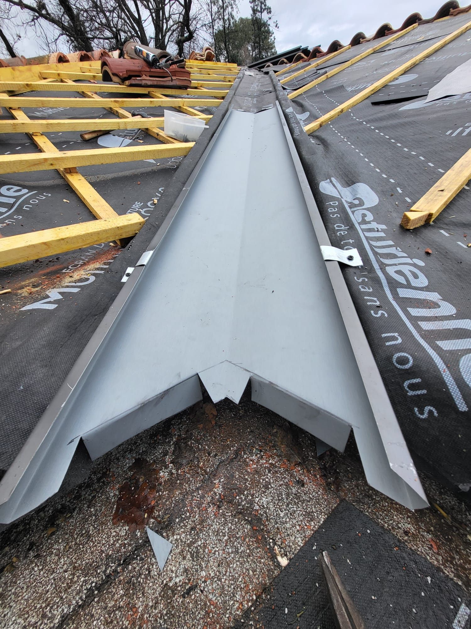 Solin de noue métallique installé sur un toit, entouré d'une sous-couche et de chevrons en bois.