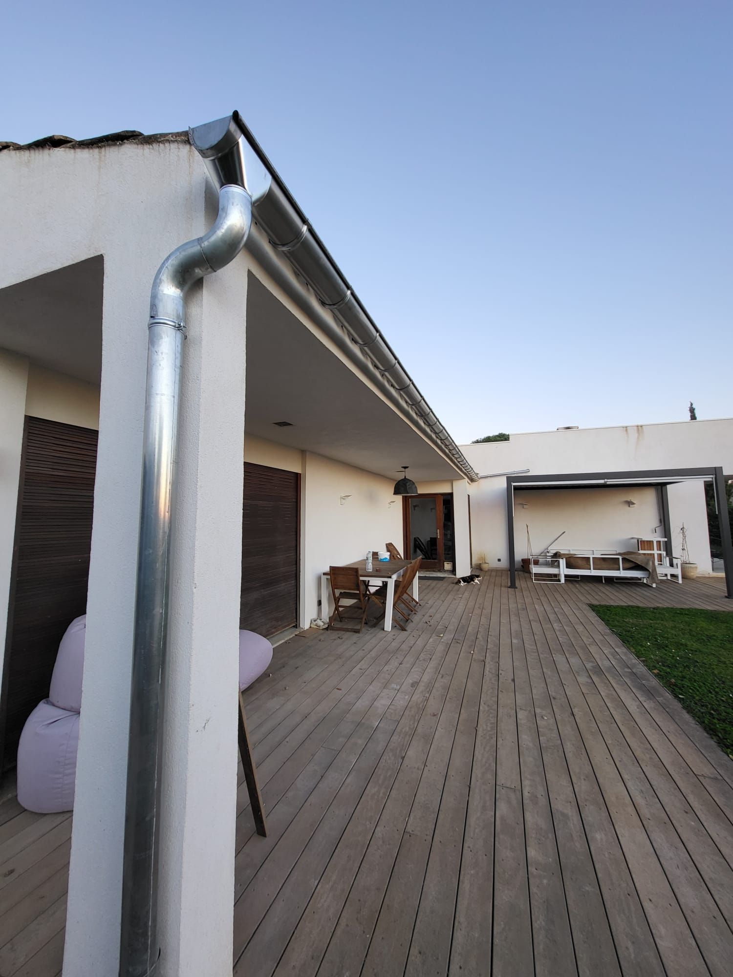 Extérieur d'une maison blanche avec terrasse en bois, équipée d'une gouttière.