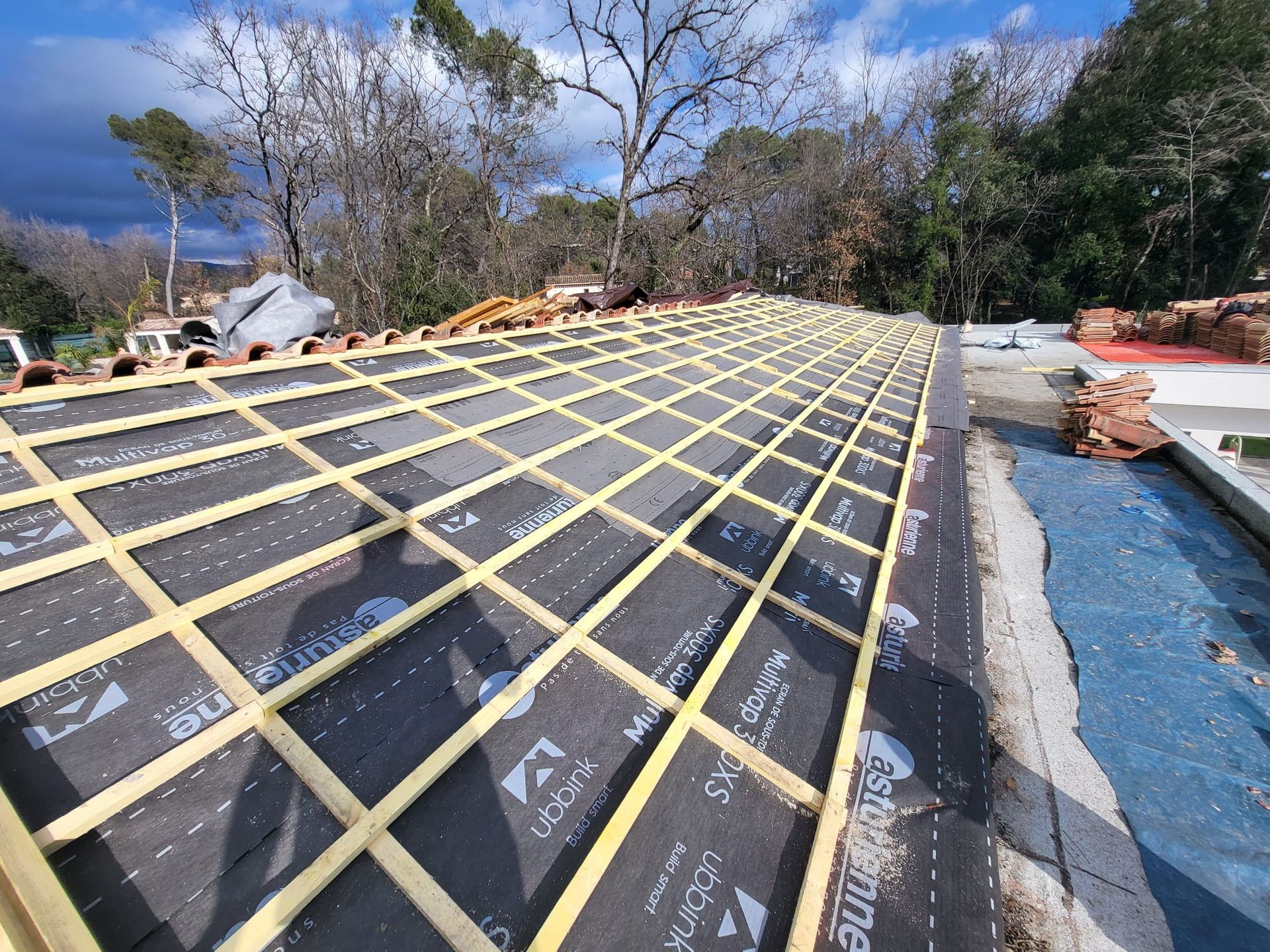 Toiture en construction ; poutres en bois et sous-couche noire ; à l'extérieur.