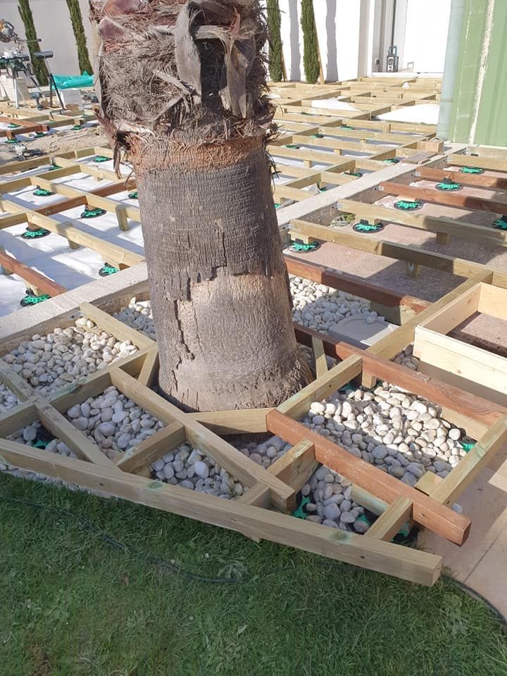 Un tronc d'arbre placé dans un pot en bois géométrique, entouré de pierres blanches et de gazon artificiel à l'intérieur