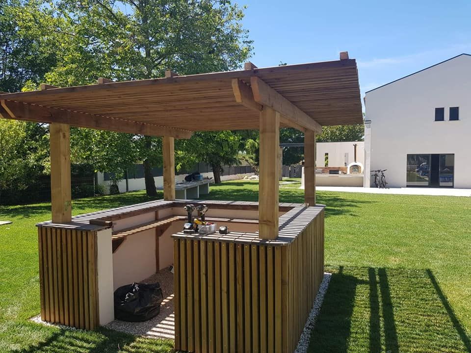 Bar extérieur en bois de style gazebo avec tabourets, installé sur une pelouse à côté d'un bâtiment blanc moderne