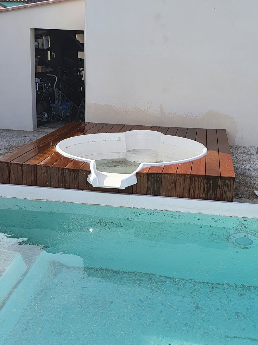 Petit jacuzzi au bord de la piscine avec terrasse en bois, jouxtant une piscine turquoise et un mur blanc