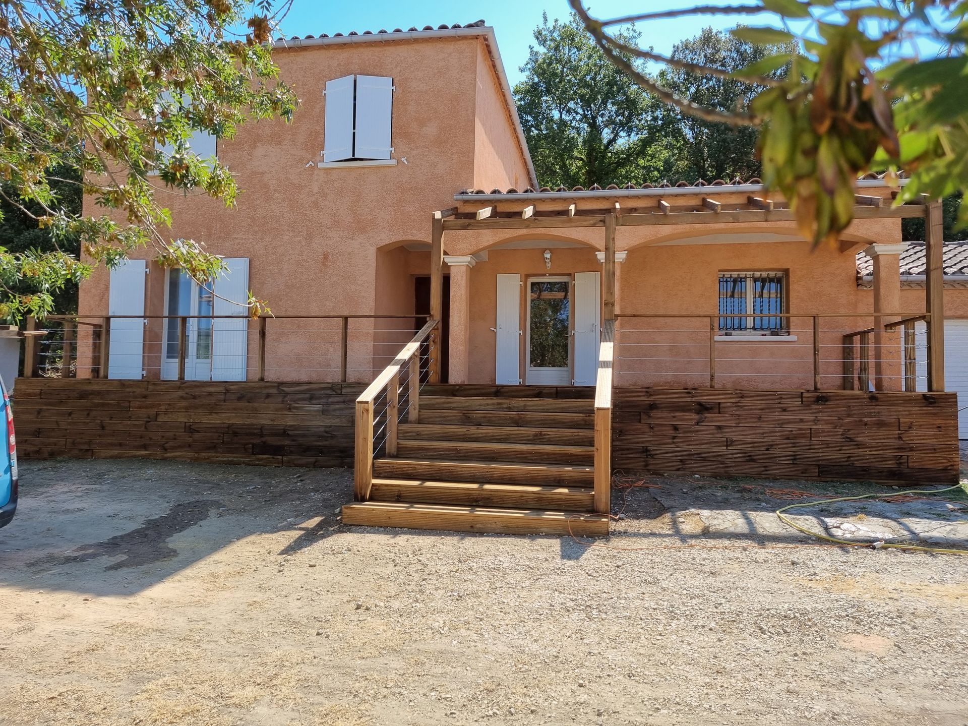 Une maison couleur pêche avec un porche, un escalier et un mur de briques dans une cour ensoleillée.