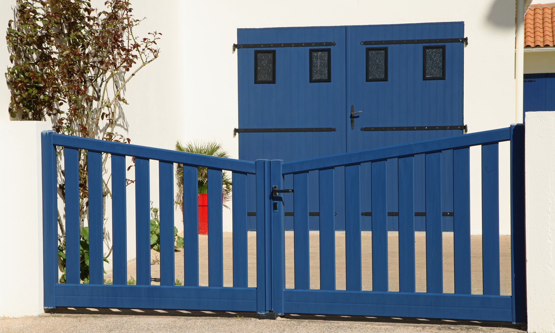 Portail et porte double bleue devant un bâtiment avec des plantes et des murs blancs