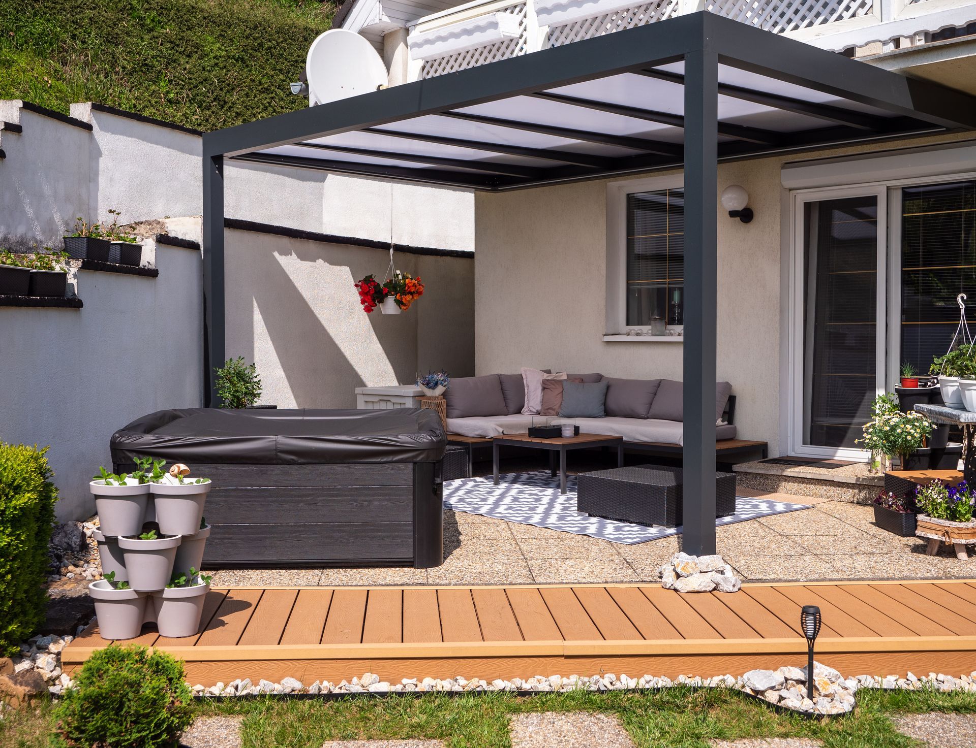 Patio moderne avec pergola, sièges en osier, tapis à motifs, terrasse en bois et plantes en pot dans un jardin
