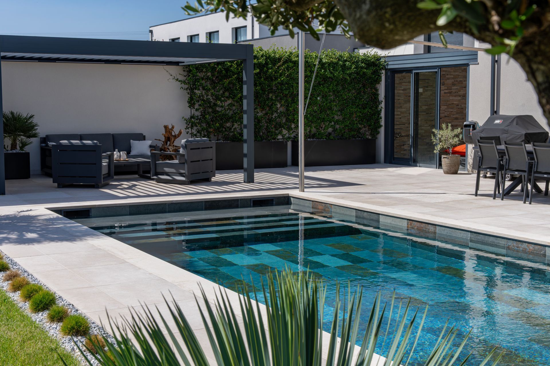 Jardin moderne avec piscine turquoise, espace détente couvert et terrasse sous une pergola