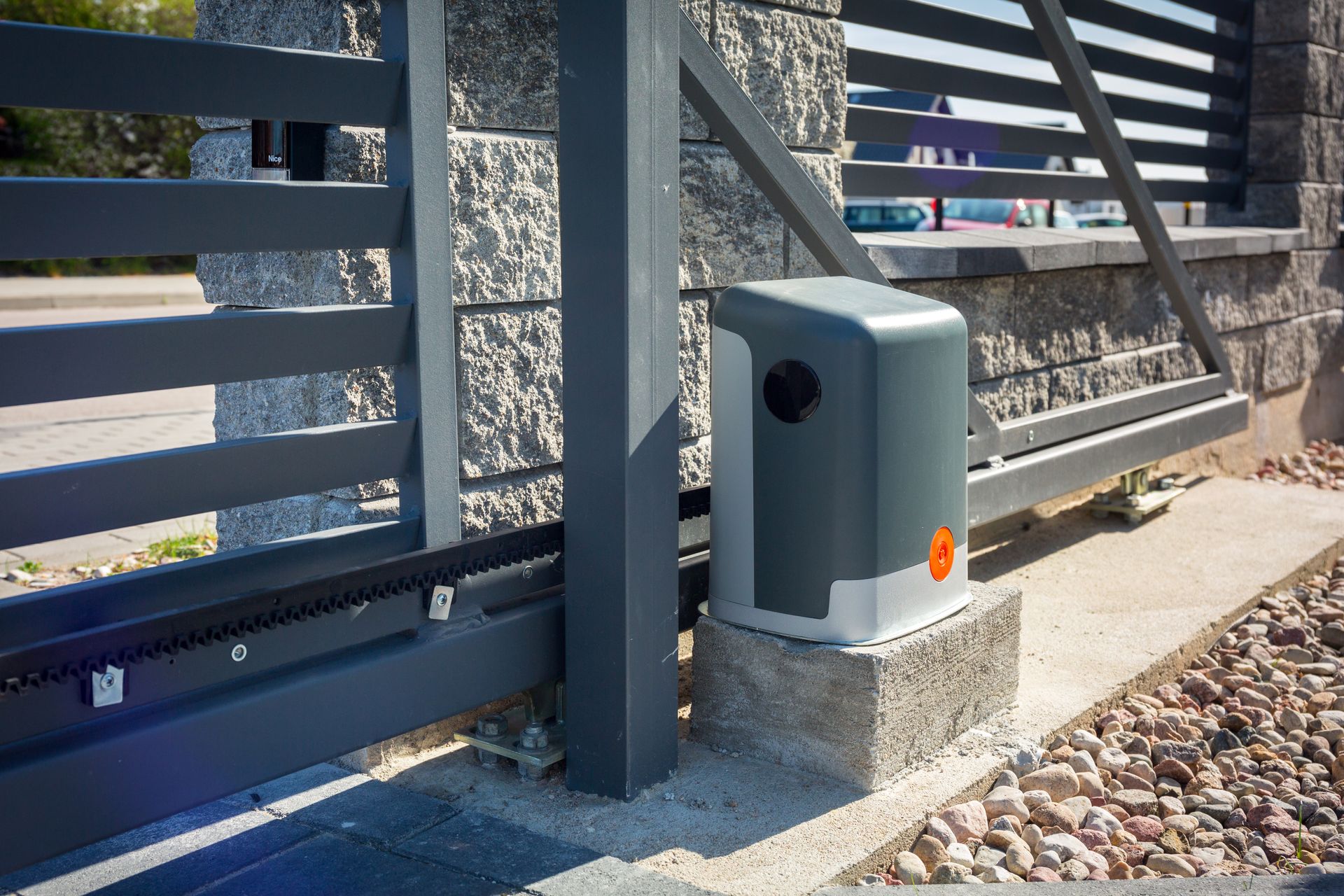 Moteur de portail automatique gris à côté d'un portail coulissant en métal foncé sur une allée de gravier