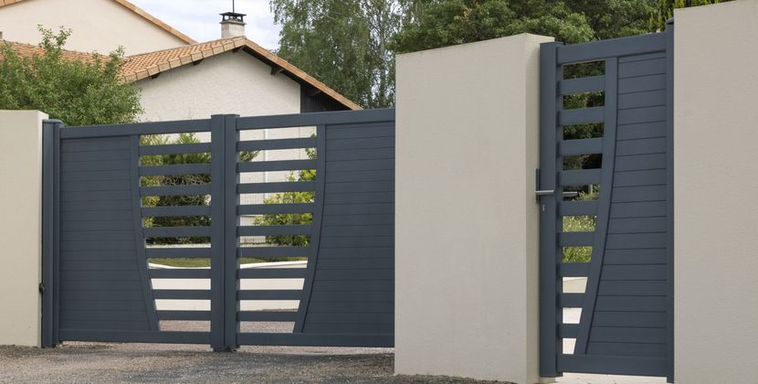 Portail d'allée moderne en métal gris foncé, jouxtant un mur et une maison en stuc clair dans un cadre suburbain