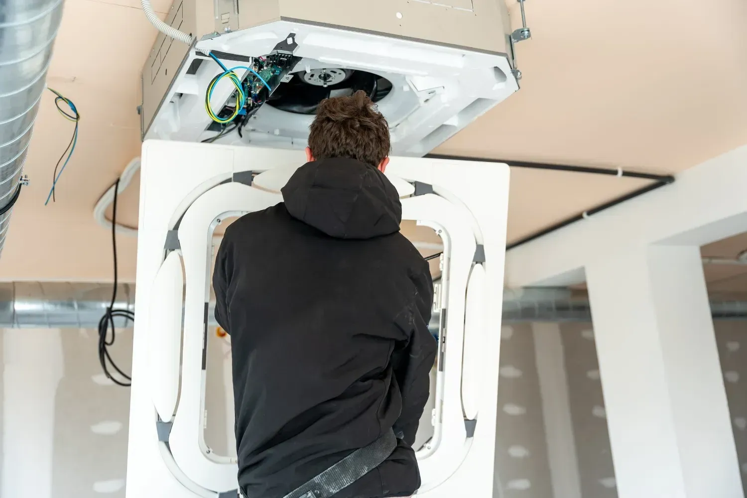 Una persona con una sudadera con capucha negra instala una unidad de climatización blanca.