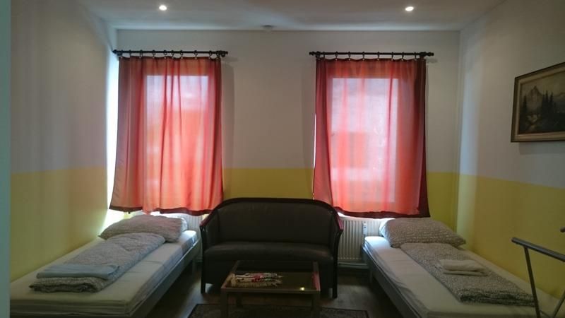 Ein Zimmer mit zwei Betten, einer Couch und zwei Fenstern.