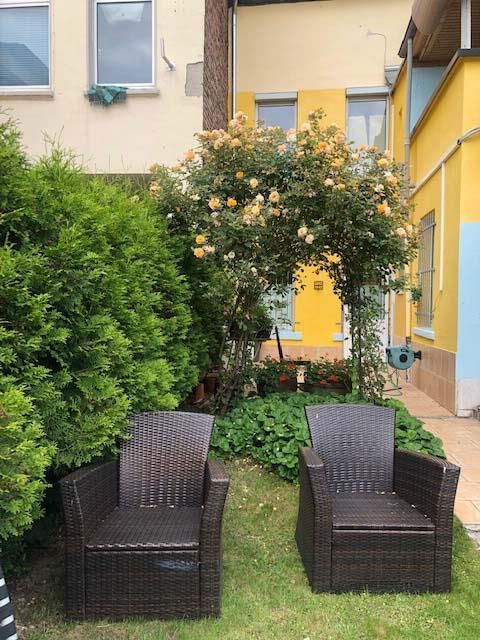 Zwei Korbstühle stehen im Gras vor einem gelben Gebäude.