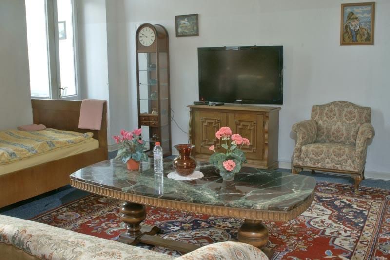 Ein Wohnzimmer mit Couch, Sessel, Uhr und Fernseher.