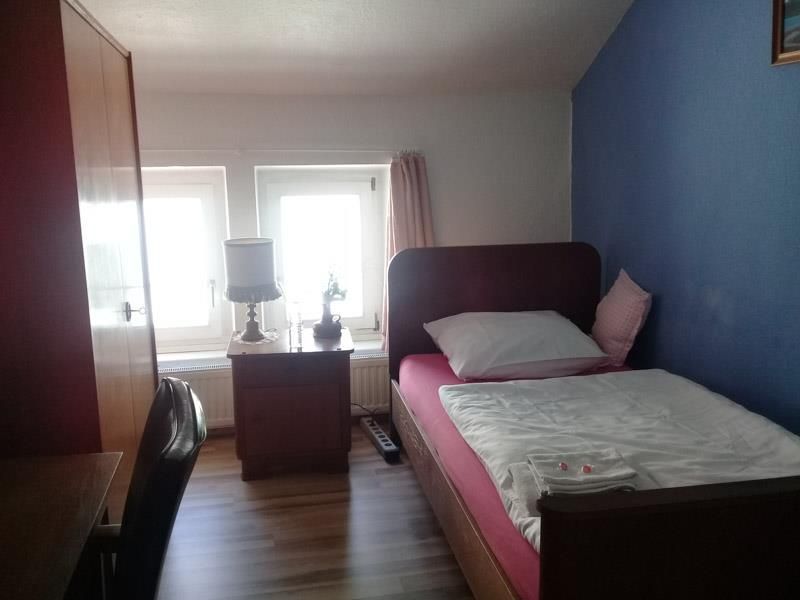Ein Schlafzimmer mit Einzelbett, Nachttisch, Lampe und Fenster.