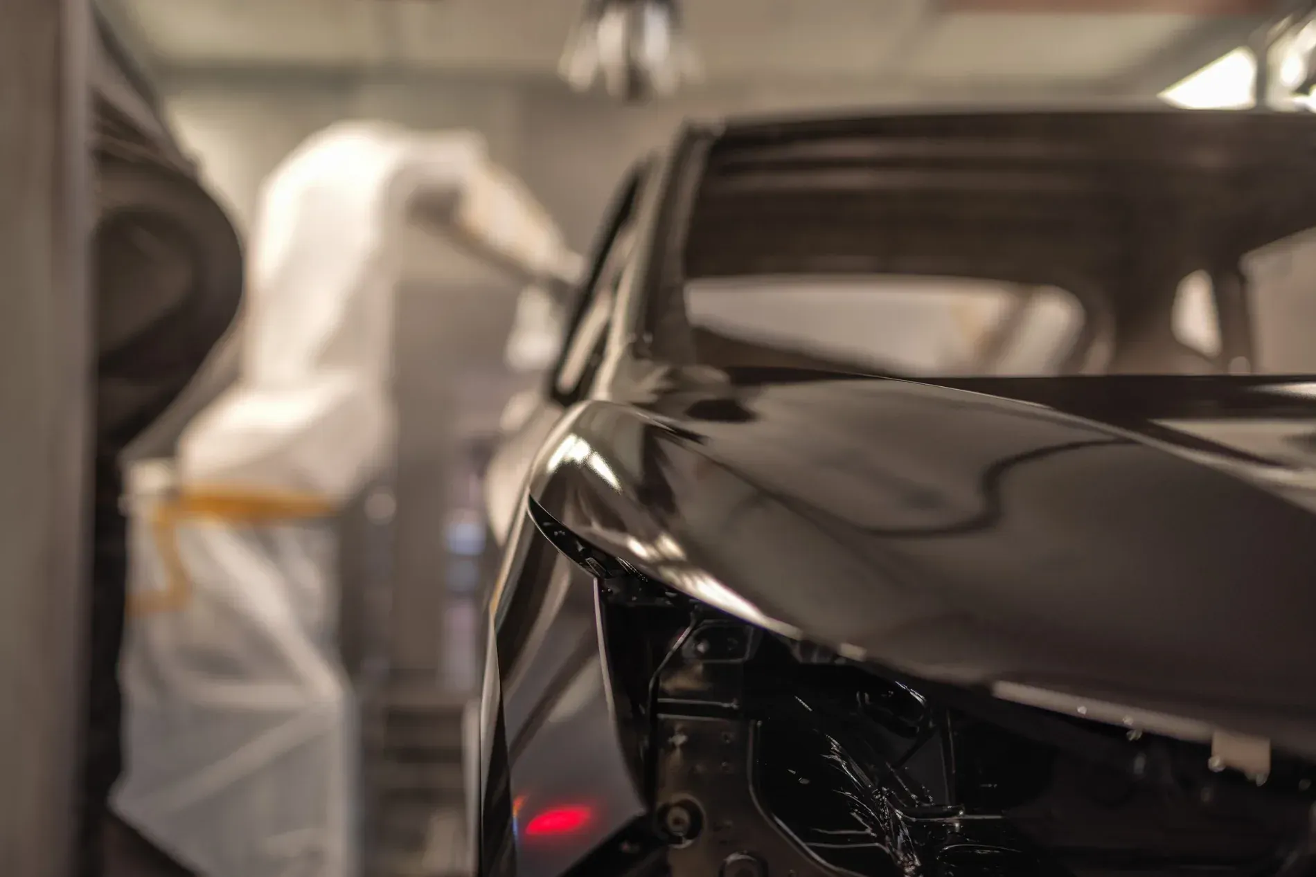 Carrocería de automóvil siendo pintada de negro por un brazo robótico en un entorno de fábrica.