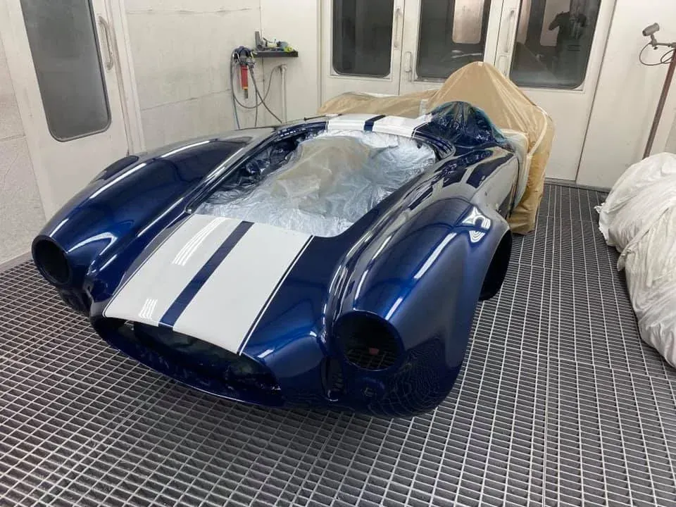 Coche deportivo clásico azul y blanco en una cabina de pintura.