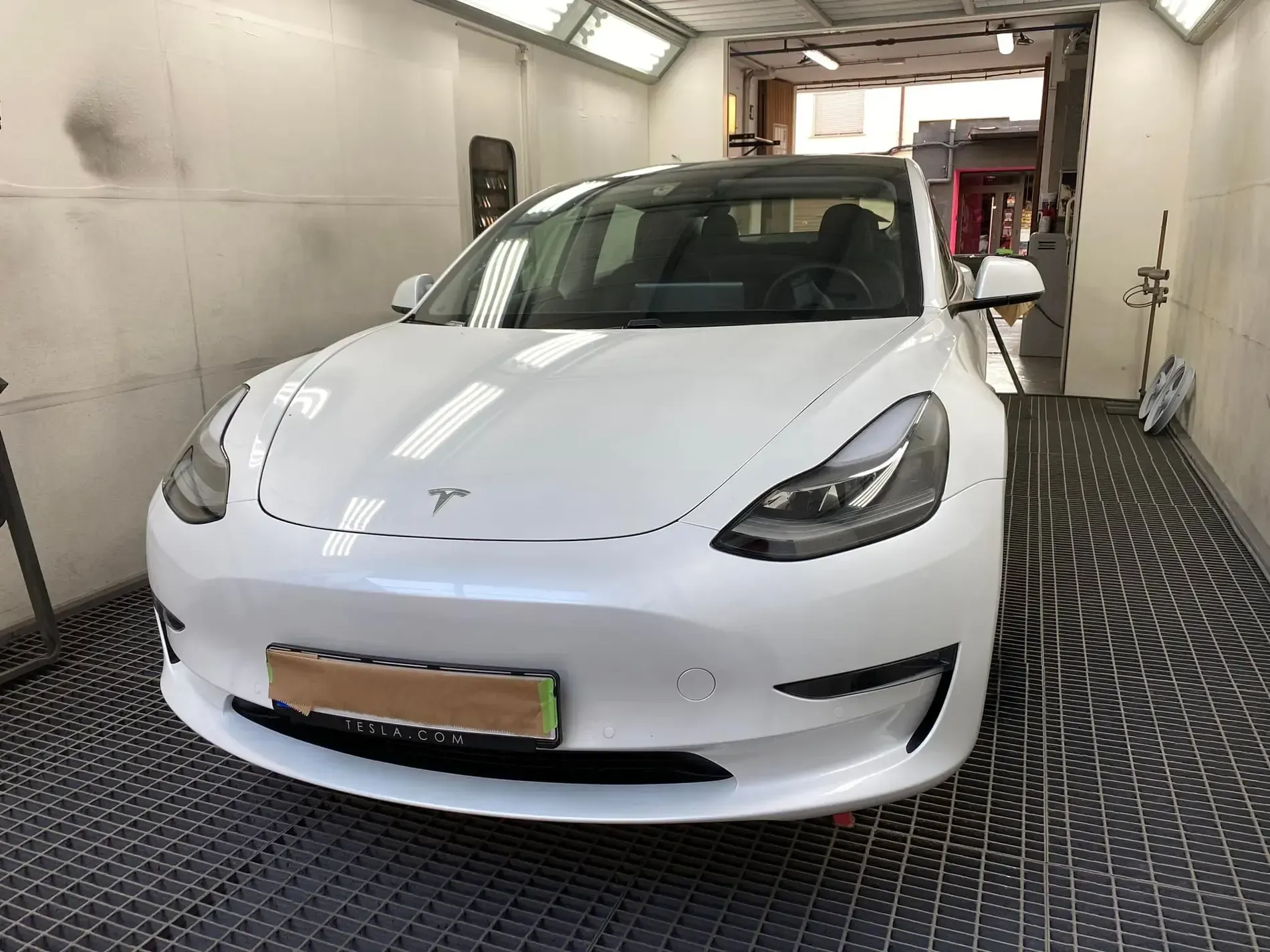 Coche Tesla de color blanco en un taller de carrocería, bajo luces brillantes, mirando a la cámara.