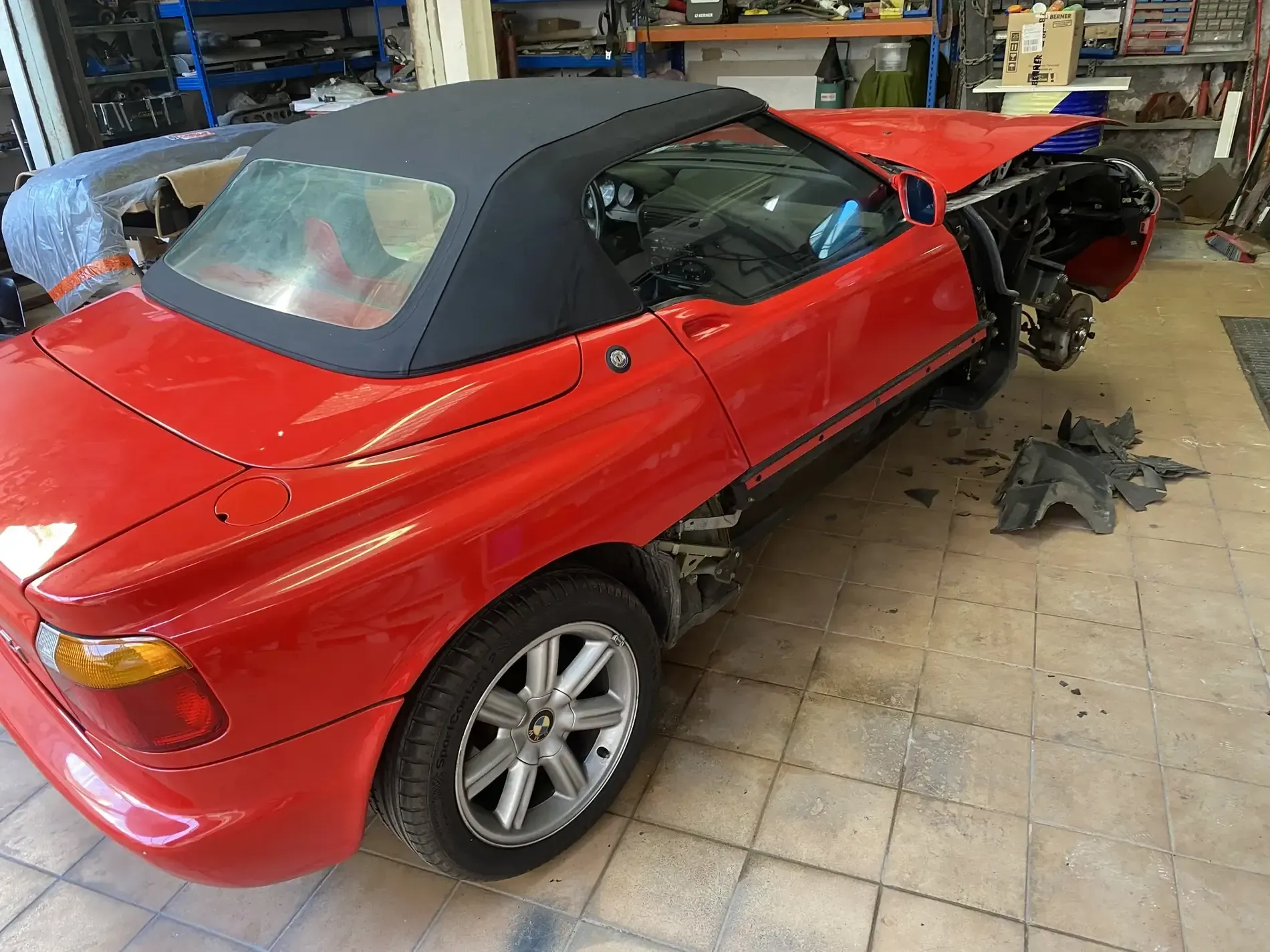 Coche descapotable de color rojo, parcialmente desmontado en taller, con capota de lona negra, falta parte delantera.