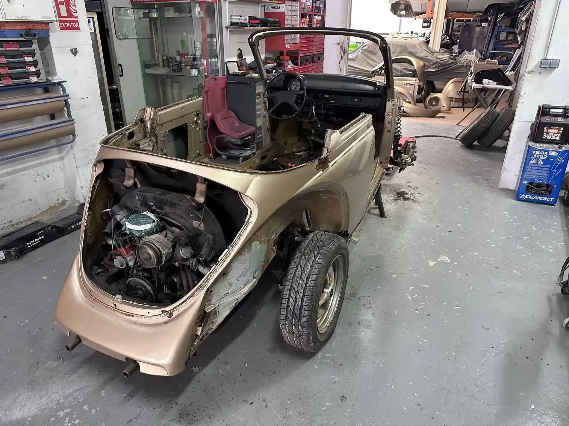 Coche antiguo dorado parcialmente montado en garaje con motor visible.