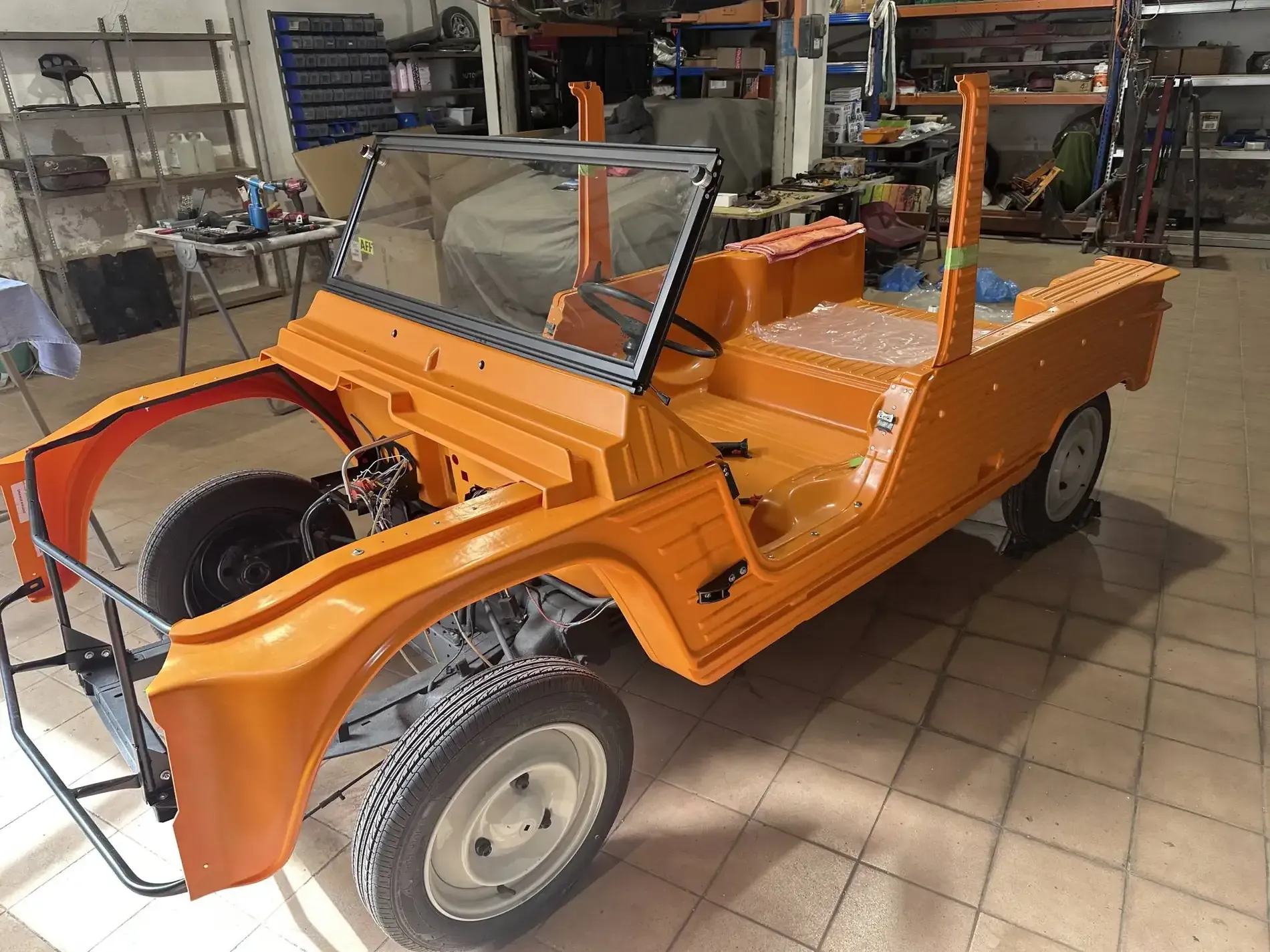 Chasis naranja de coche clásico en taller, en restauración. Parachoques delantero y llantas negros.