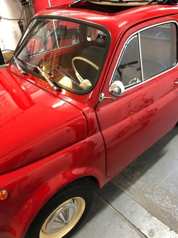 Coche clásico Fiat 500 de color rojo con neumáticos con llantas blancas, techo corredizo y espejo lateral cromado.