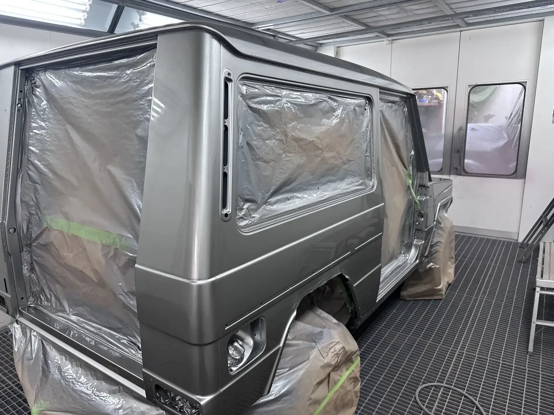 Carrocería gris enmascarada en cabina de pintura, lista para pintar.