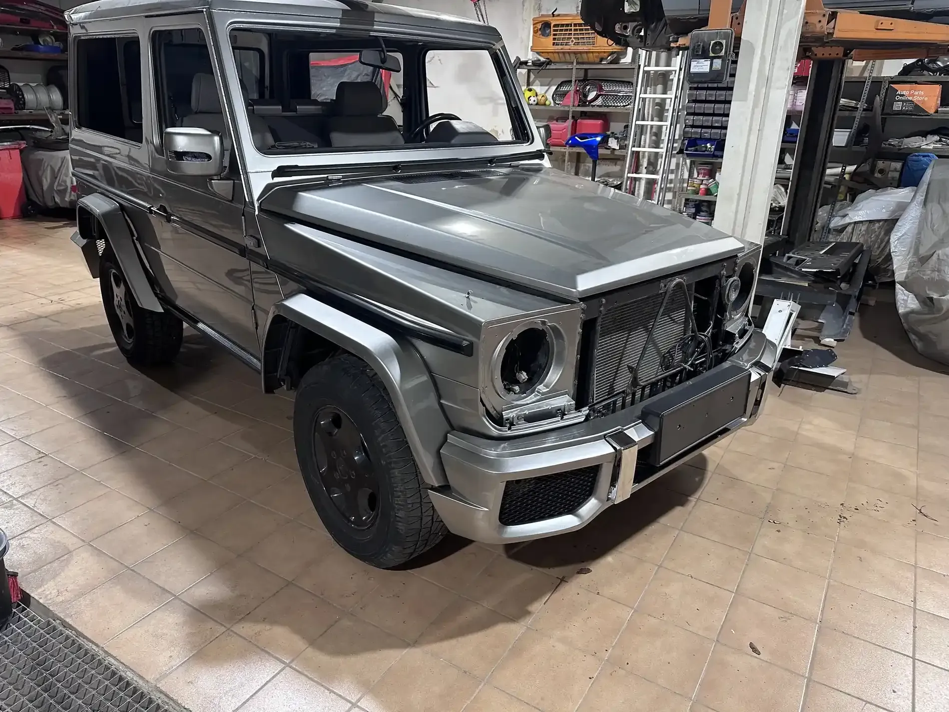 SUV Mercedes-Benz Clase G de color gris en un taller, sin parrilla delantera ni faros.