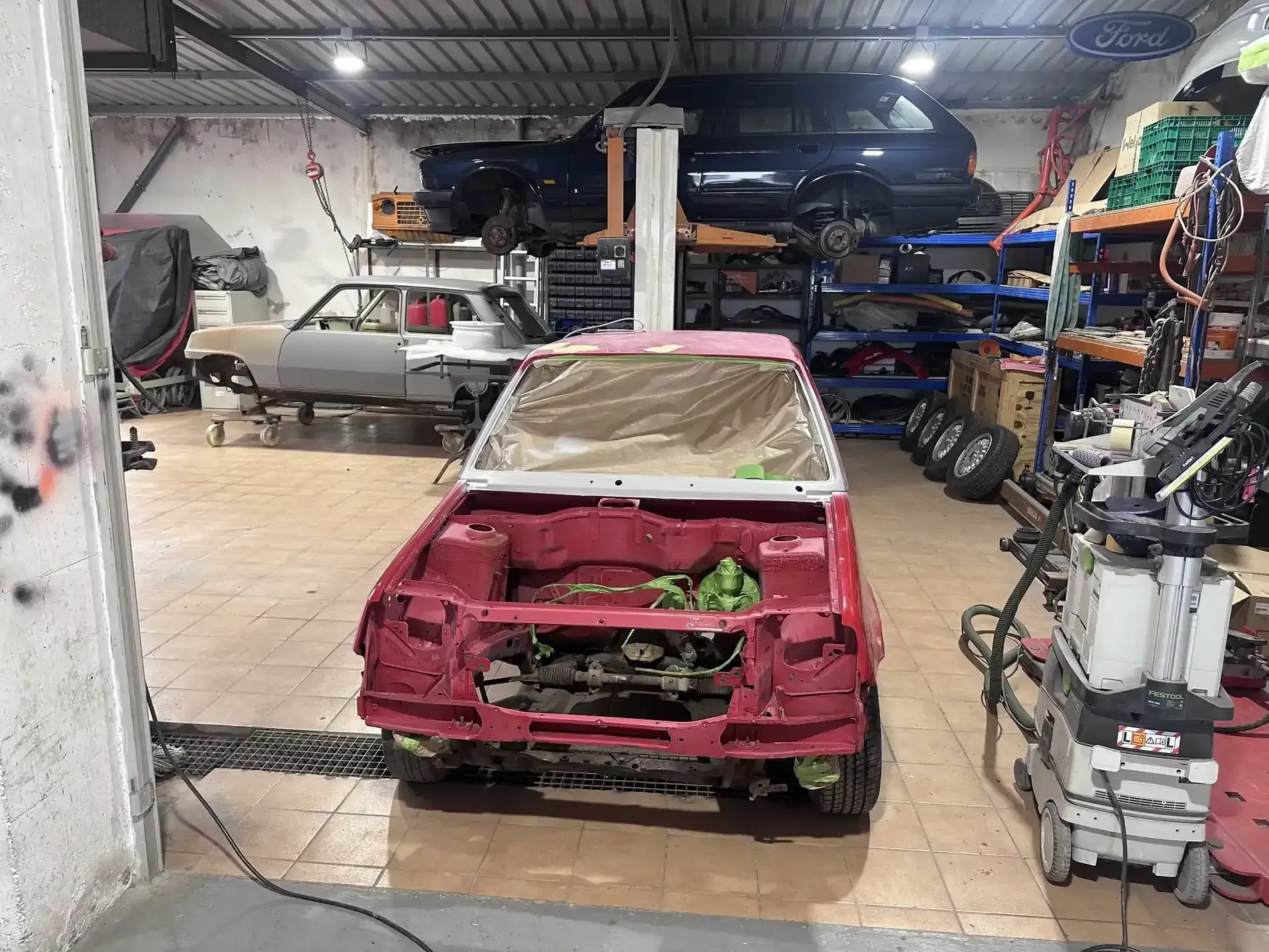 Una carrocería roja en un taller, en proceso de restauración. Un papel protector cubre el parabrisas.