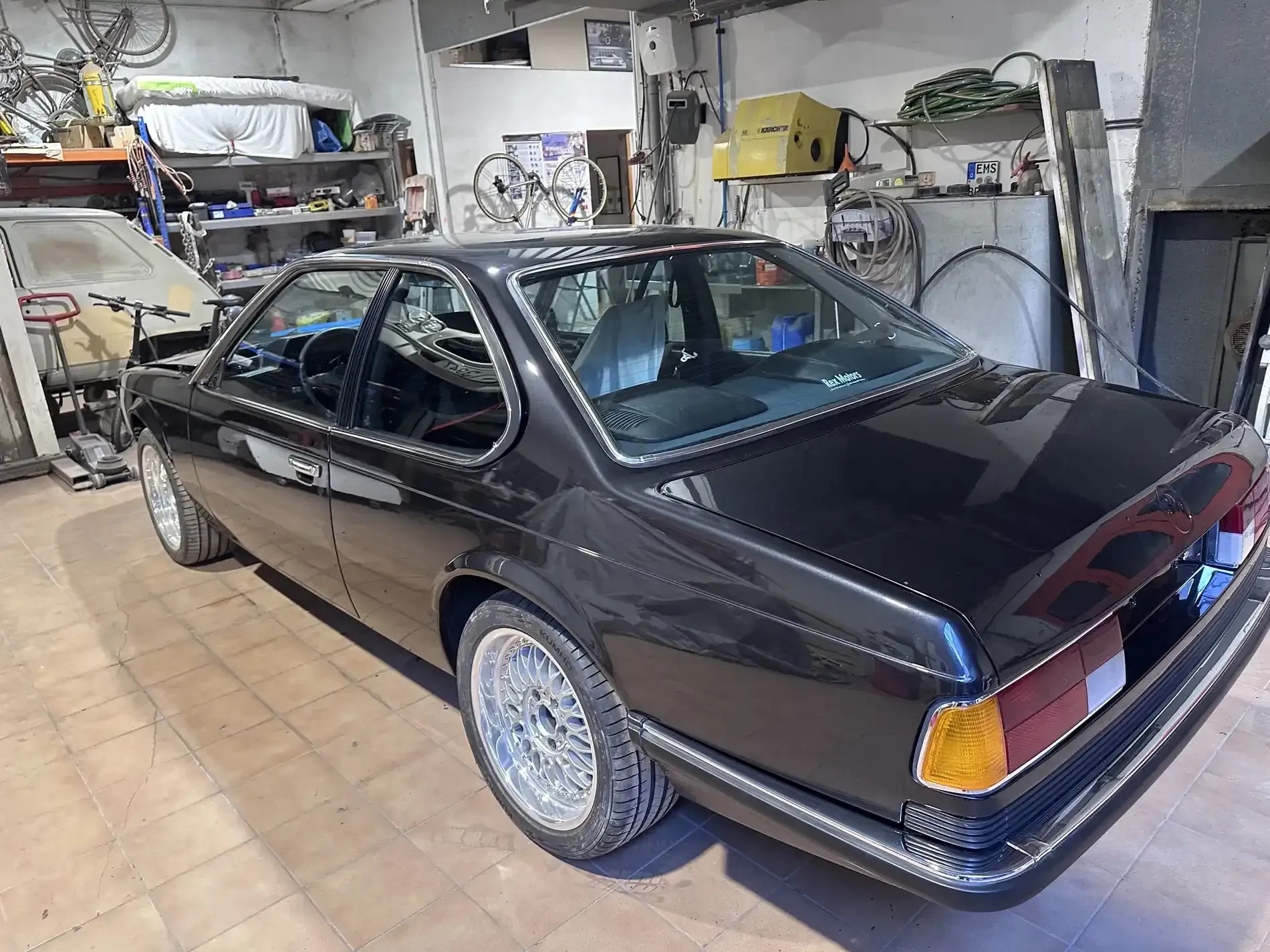 BMW coupé clásico negro en un taller con ruedas plateadas.