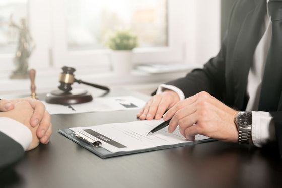 Un abogado está sentado en un escritorio con un cliente y firma un documento.