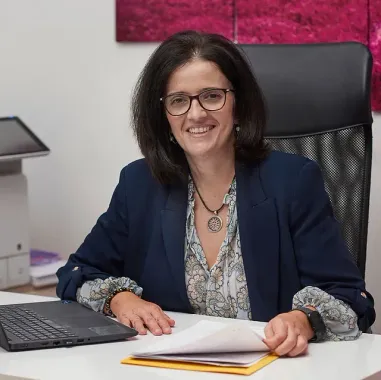 Mujer sonriendo en un escritorio con una computadora portátil y papeles en una oficina.