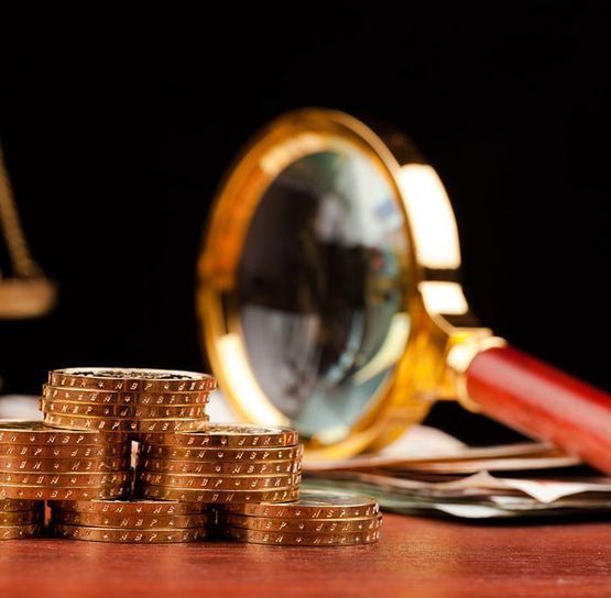 Monedas de oro apiladas junto a una lupa sobre un escritorio.