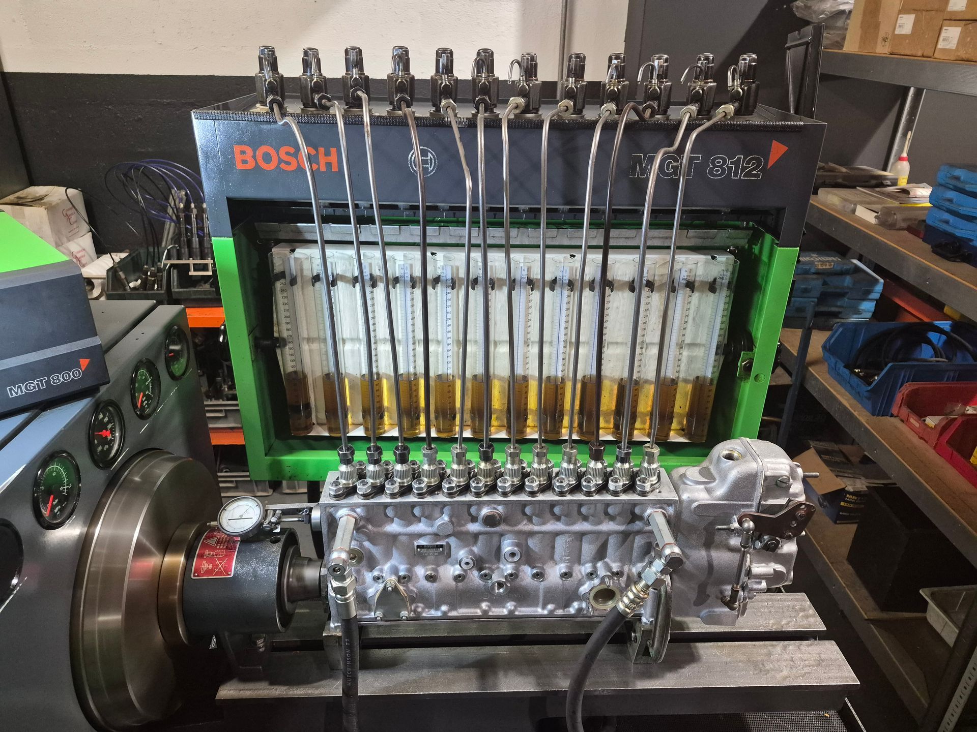 Pompe d'injection de carburant diesel sur une machine d'essai Bosch, avec des tubes remplis de liquide ambré dans un garage.
