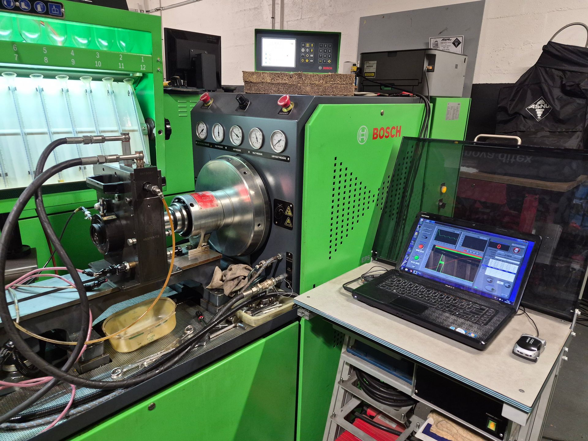 Une pompe à injection diesel sur un banc d'essai Bosch, avec un ordinateur portable affichant les diagnostics.