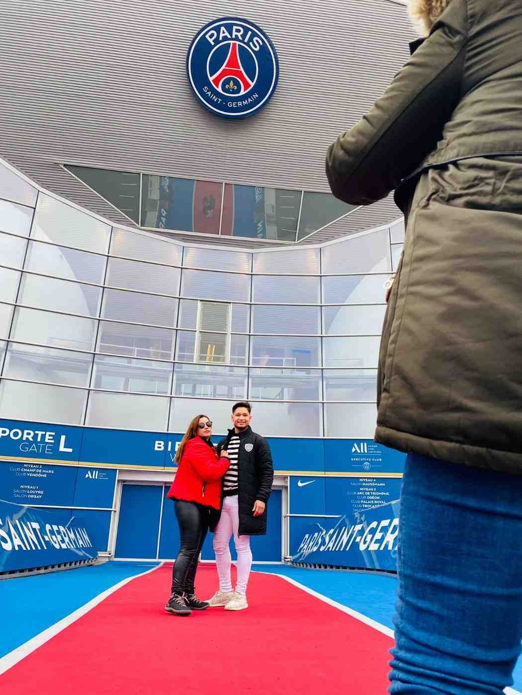 Pareja posando frente al logo del Paris Saint-Germain en un estadio.