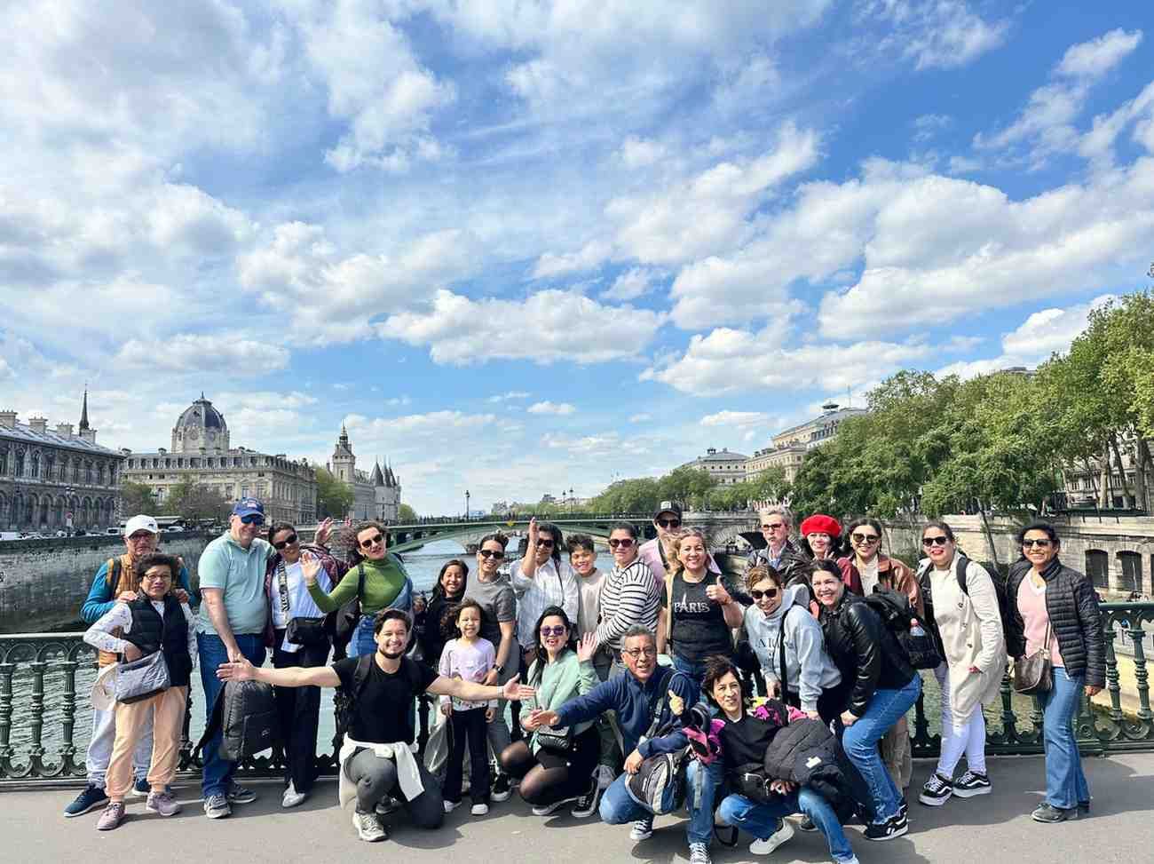 Un gran grupo de personas posando en un puente en París, Francia. Al fondo se ven edificios y el cielo.