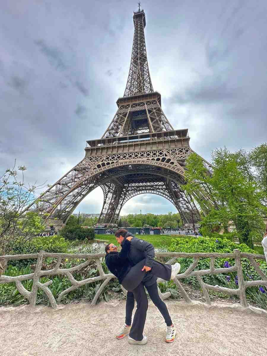 Pareja besándose frente a la Torre Eiffel. Un hombre abraza a una mujer en un chapuzón. Cielo nublado.