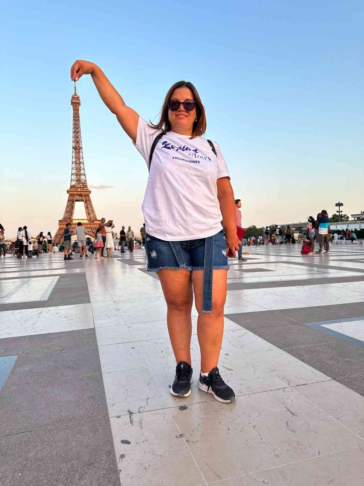Mujer con el brazo levantado frente a la Torre Eiffel.
