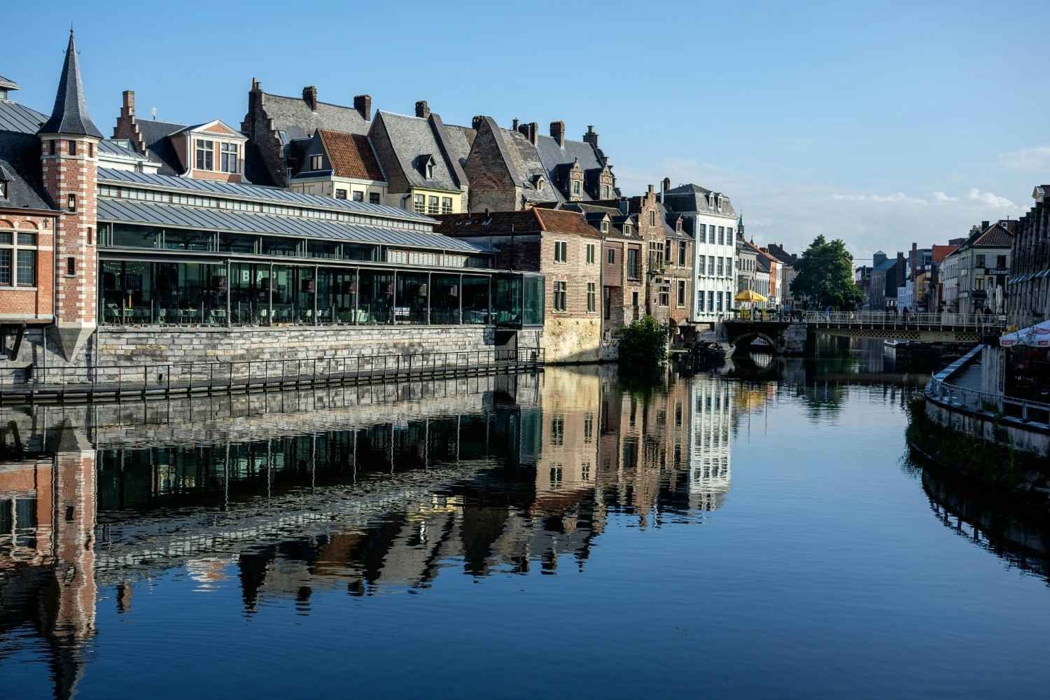 Los edificios bordean un canal, reflejándose en el agua, bajo un cielo azul en una ciudad europea.
