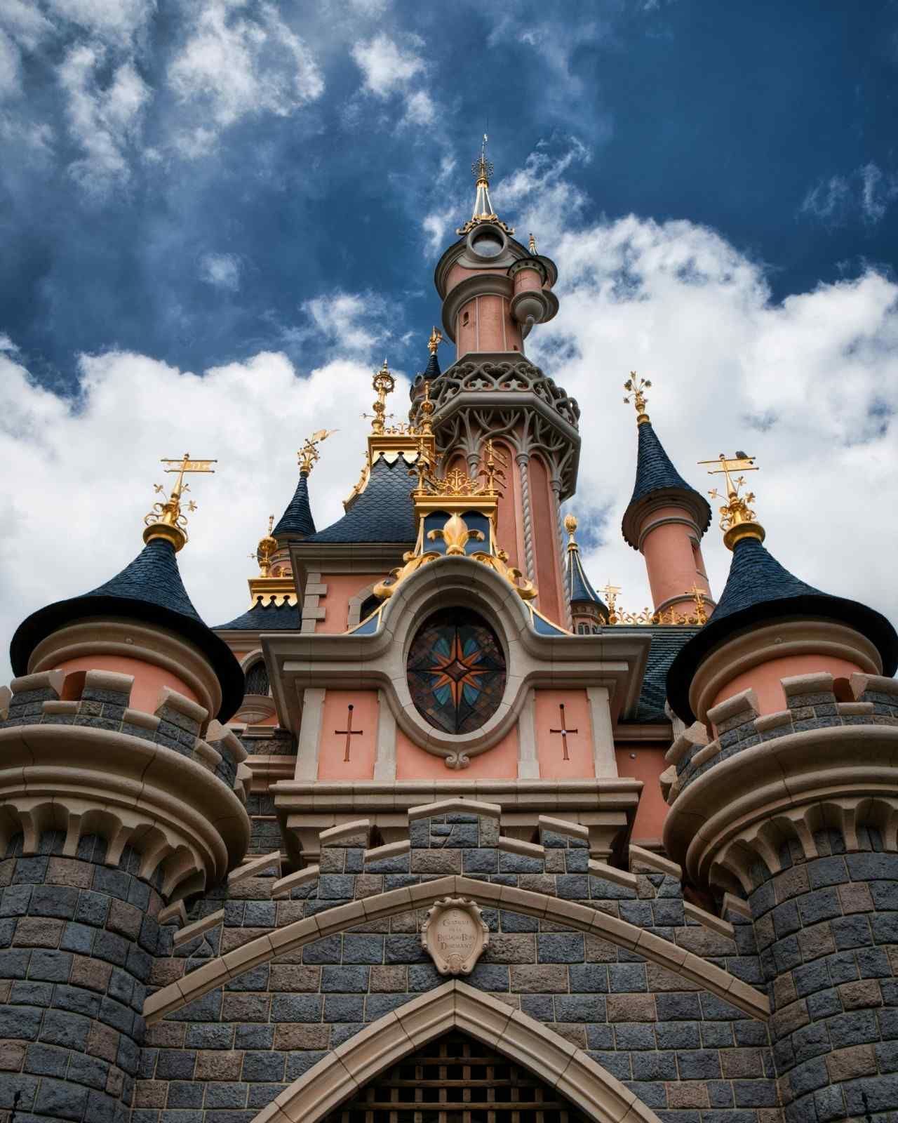 Castillo de la Bella Durmiente en Disneyland París, piedra rosa y gris, cielo azul, acentos dorados.