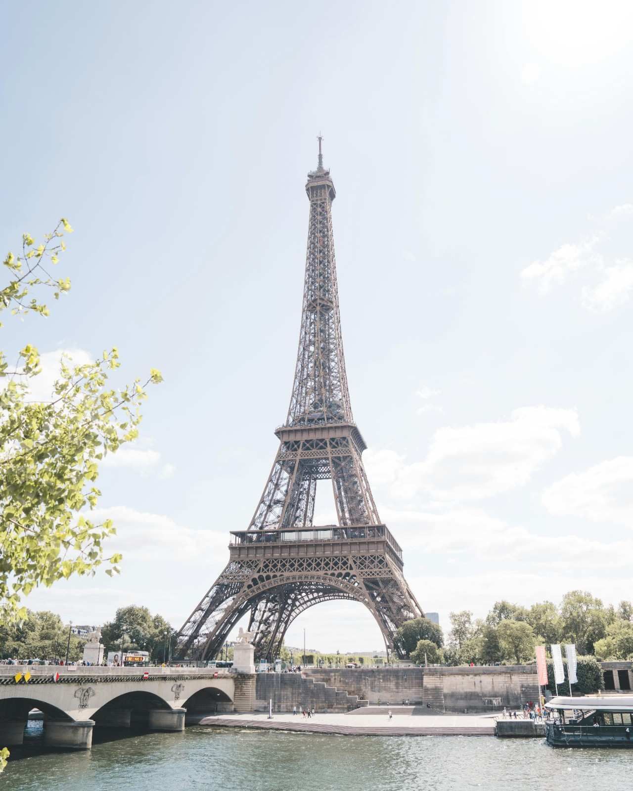 La Torre Eiffel en París, Francia, se eleva contra un cielo azul brillante, con el río Sena en primer plano.