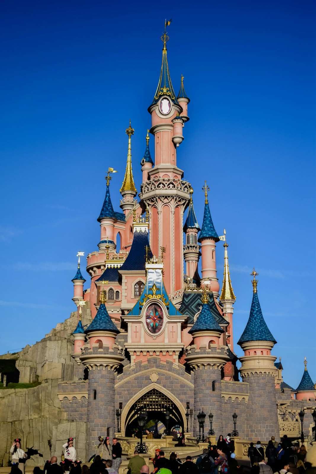 Castillo de la Bella Durmiente en Disneyland París, torres rosas y azules contra un cielo azul claro.