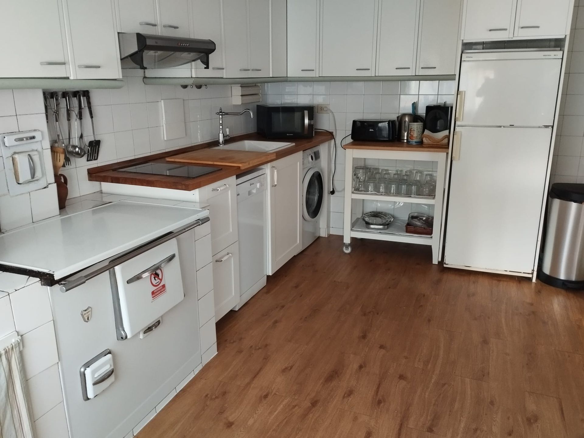 Cocina blanca con gabinetes, electrodomésticos, encimera de madera y piso laminado.
