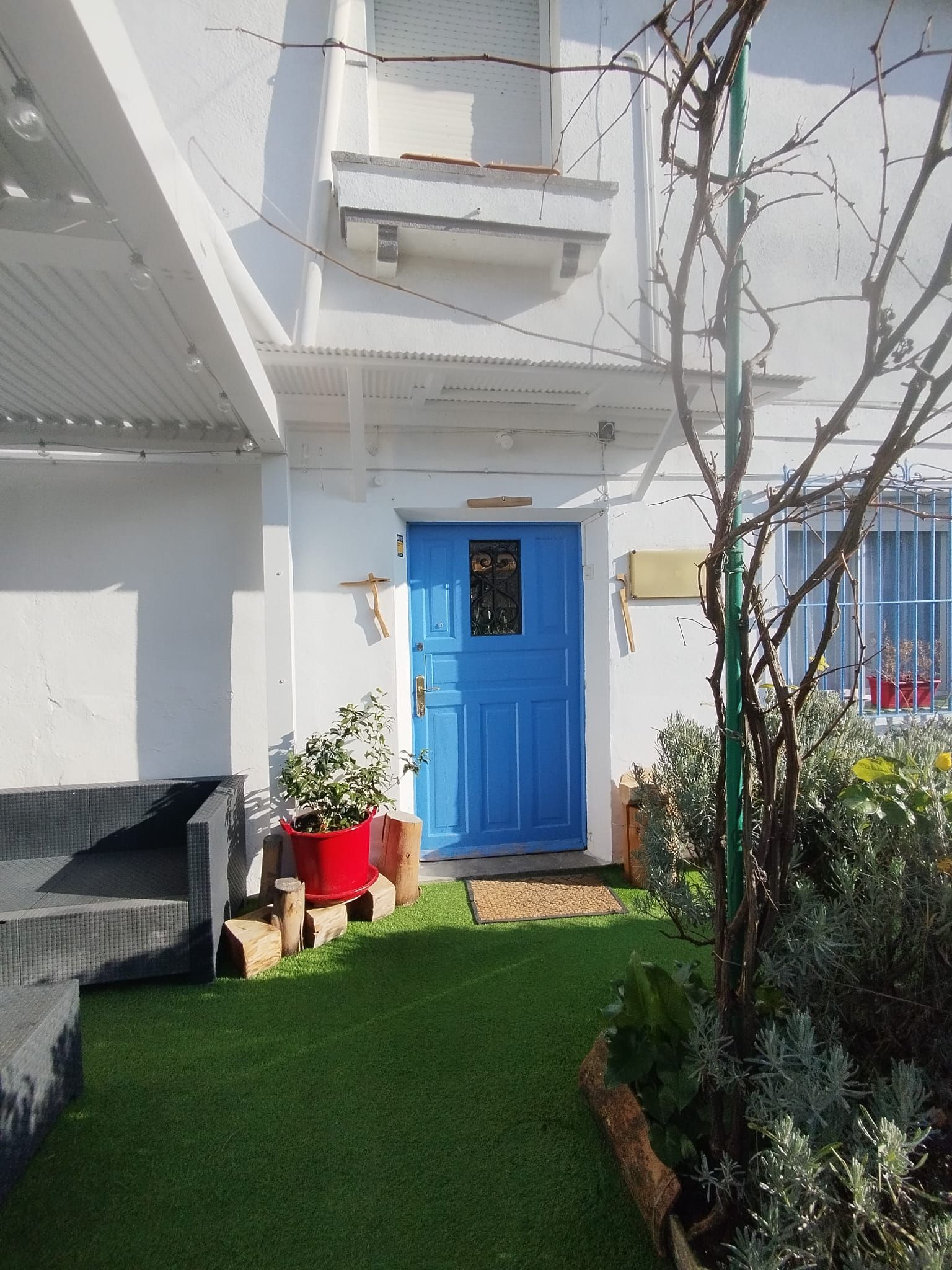 Puerta de entrada azul, fachada blanca. Césped verde, pequeño jardín.