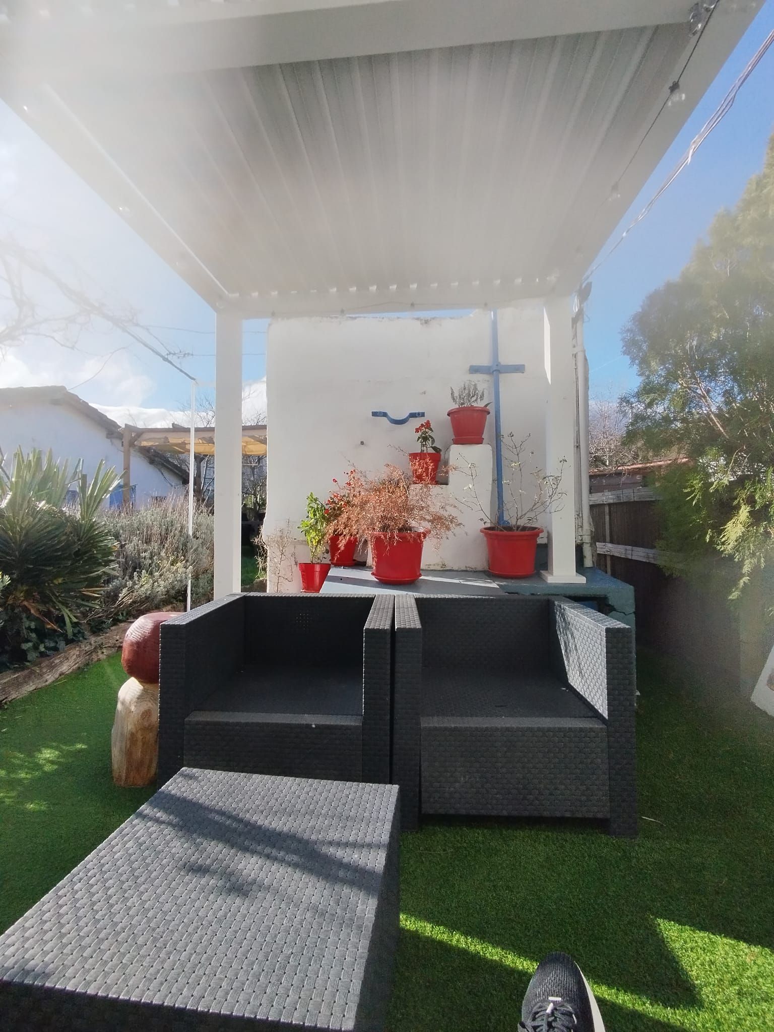 Zona de estar en el patio con muebles negros, plantas en macetas rojas y dosel blanco.