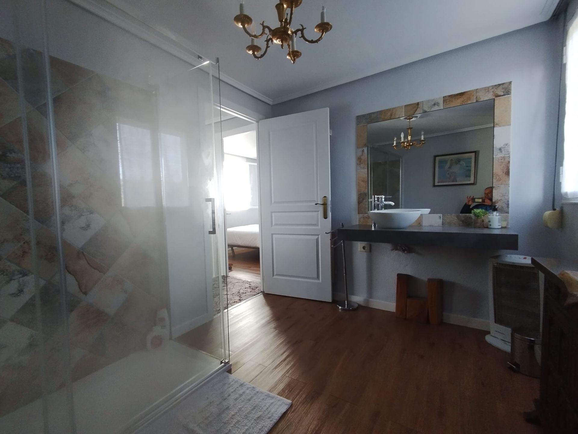 Baño con ducha, lavabo y puerta abierta al dormitorio con luz natural.